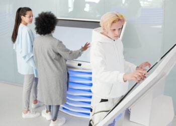 Drei Personen bedienen interaktive Touch-Terminals und ein grosses Display in einem hellen Bueroumfeld