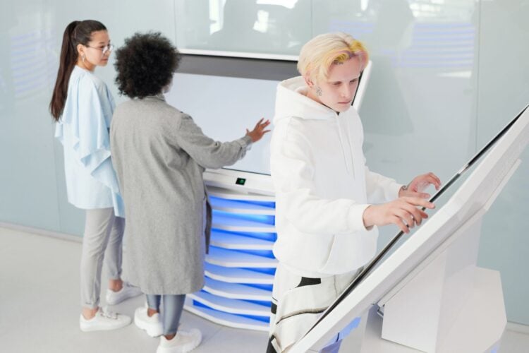 Drei Personen bedienen interaktive Touch-Terminals und ein grosses Display in einem hellen Bueroumfeld