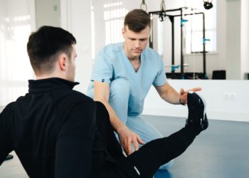 Physiotherapeut betreut einen Patienten bei einer Beinuebung in einer hellen Praxis