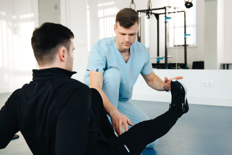 Physiotherapeut betreut einen Patienten bei einer Beinuebung in einer hellen Praxis