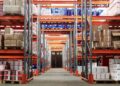 Weitwinkelansicht einer Logistikhalle mit gefüllten Hochregalen und Kartons