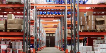 Weitwinkelansicht einer Logistikhalle mit gefüllten Hochregalen und Kartons