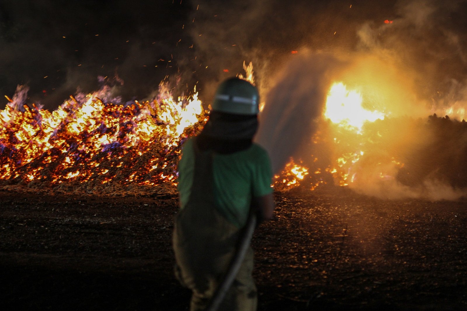 Ein Feuerwehrmann vor einem in Vollbrand stehenden Holzpolter