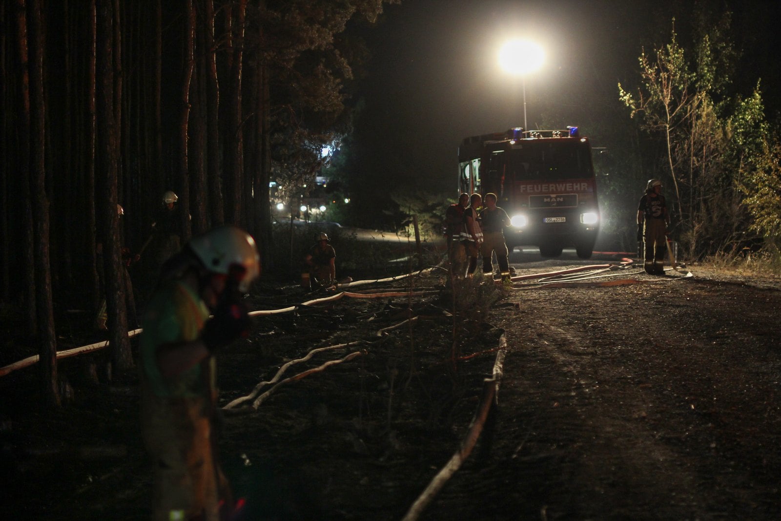 Einsatzkräfte und ein Löschfahrzeug auf einem Waldweg bei Nacht