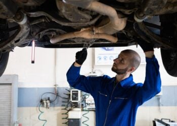 Mechaniker im blauen Overall arbeitet unter einem aufgebockten Auto an der Abgasanlage