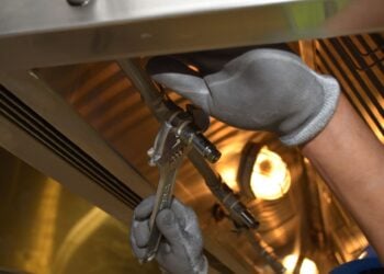 Handwerker mit Arbeitshandschuhen montiert mit einer Rohrzange eine Verbindung an einer Armatur