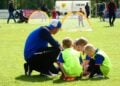 Trainer kniet beim Bambini-Training vor vier Kindern in Leibchen