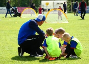 Trainer kniet beim Bambini-Training vor vier Kindern in Leibchen
