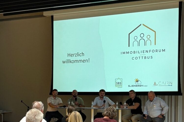 Fünf Männer sitzen auf einem Podium vor einer Leinwand mit dem Schriftzug Immobilienforum Cottbus