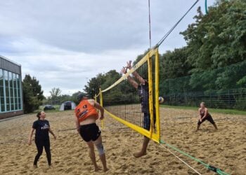 Beachvolleyballerinnen und -volleyballer am Netz auf einem Sandfeld