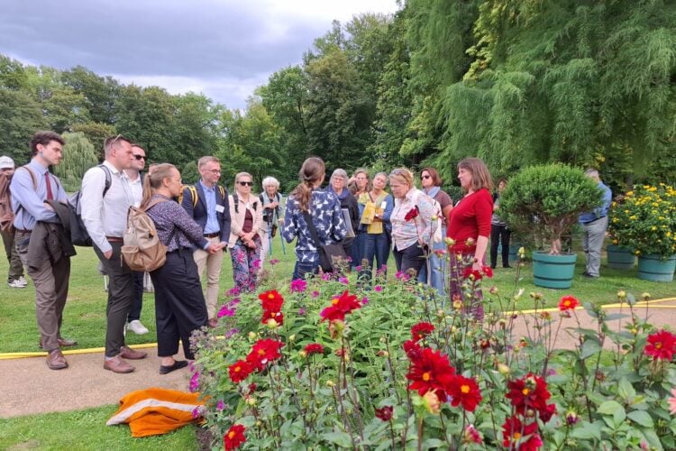 Tagungsteilnehmer stehen bei einer Führung vor einem Blumenbeet im Park