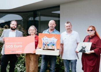 Fünf Personen mit Spendenscheck und einem selbst gebauten Puppentheater vor dem Kinderhaus