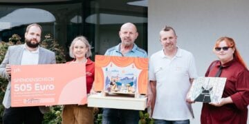 Fünf Personen mit Spendenscheck und einem selbst gebauten Puppentheater vor dem Kinderhaus