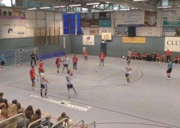 Handballspiel in einer Sporthalle, Spieler in roten und weißen Trikots im Angriff
