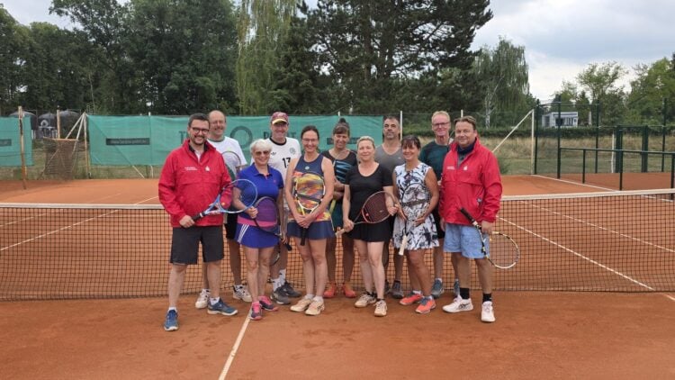 Tennisspielerinnen und -spieler stehen mit Schlägern vor dem Netz auf dem Sandplatz