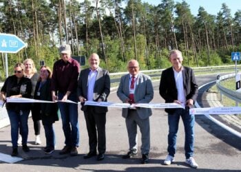 Sieben Personen durchschneiden ein Band auf der neuen Auffahrt zur A117, im Hintergrund Kiefernwald