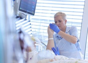 Physiotherapeutin bewegt die Hand einer Patientin auf der Intensivstation