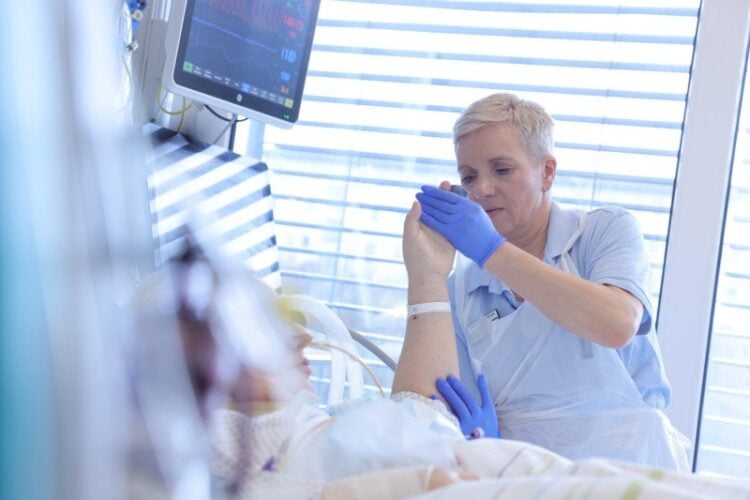 Physiotherapeutin bewegt die Hand einer Patientin auf der Intensivstation