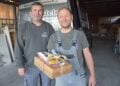 Zwei Männer in Arbeitskleidung stehen vor einem Firmenfahrzeug
