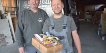 Zwei Männer in Arbeitskleidung stehen vor einem Firmenfahrzeug