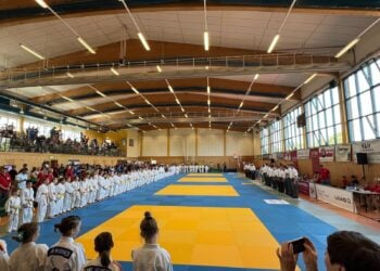 Junge Judoka in weißen Anzügen stehen zur Eröffnung um die Wettkampfmatte in einer Sporthalle