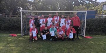 Fußballmannschaft in roten Trikots mit Urkunden und Pokal vor einem Tor
