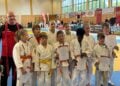 Kindergruppe in weißen Judoanzügen mit Urkunden in einer Sporthalle