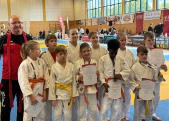 Kindergruppe in weißen Judoanzügen mit Urkunden in einer Sporthalle