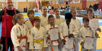 Kindergruppe in weißen Judoanzügen mit Urkunden in einer Sporthalle