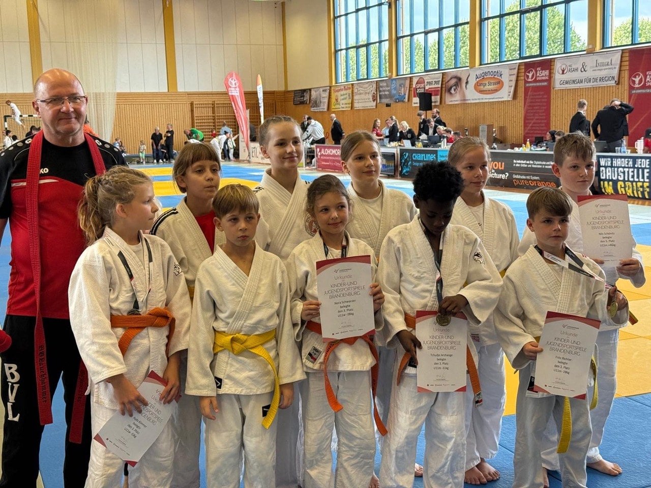 Kindergruppe in weißen Judoanzügen mit Urkunden in einer Sporthalle