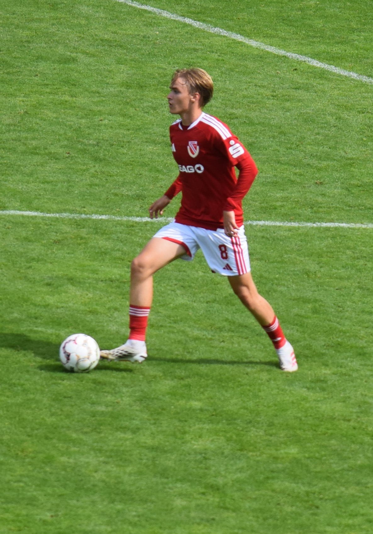 Fußballspieler in rotem Trikot am Ball auf dem Rasen