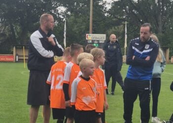 Kinder in orangen Leibchen mit Trainern am Spielfeldrand