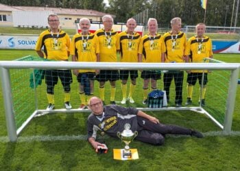 Acht Fußballer in gelb-schwarzen Trikots vor einem Tor, davor ein Spieler mit Pokal