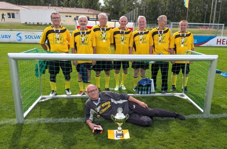 Acht Fußballer in gelb-schwarzen Trikots vor einem Tor, davor ein Spieler mit Pokal
