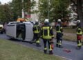 Auf der Seite liegendes Auto und Einsatzkräfte der Feuerwehr in einer Wohnstraße