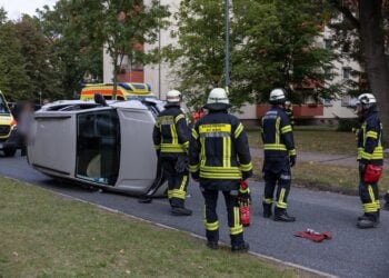 Auf der Seite liegendes Auto und Einsatzkräfte der Feuerwehr in einer Wohnstraße