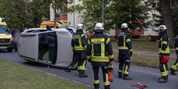 Auf der Seite liegendes Auto und Einsatzkräfte der Feuerwehr in einer Wohnstraße