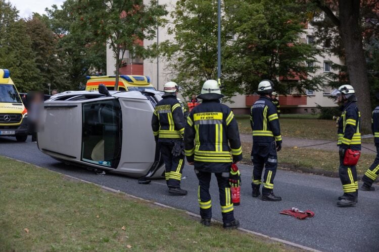 Auf der Seite liegendes Auto und Einsatzkräfte der Feuerwehr in einer Wohnstraße