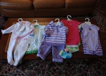 Neue Babykleidung mit Preisschildern liegt auf einem Tisch ausgebreitet
