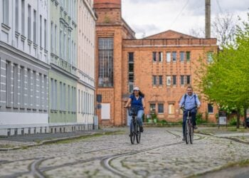 Radfahrende auf einem Weg entlang historischer Industriebauten