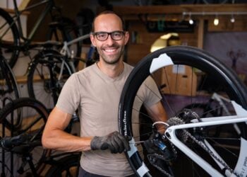 Mann mit Brille hält in einer Fahrradwerkstatt ein Rennrad-Laufrad in den Händen