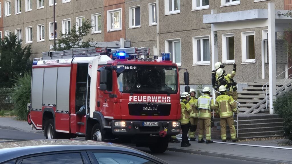 Feuerwehrleute mit Atemschutz vor dem Eingang eines Plattenbaus