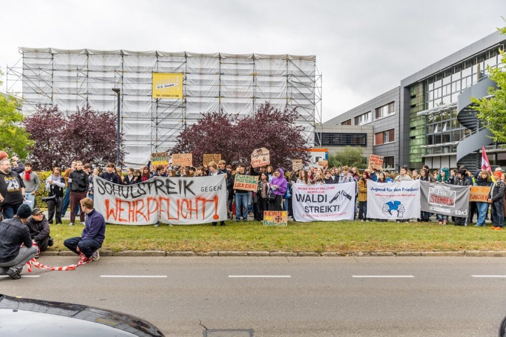 Schülerinnen und Schüler stehen mit Transparenten gegen die Wehrpflicht am Straßenrand in Cottbus