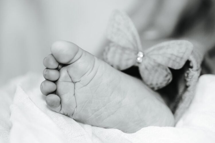 Symbolbild Sternenkinder, schwarz-weiße Nahaufnahme eines Babyfußes neben einem Stoffschmetterling