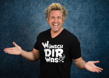 Sascha Grammel im schwarzen T-Shirt mit der Aufschrift Wünsch Dir Was, lachend mit ausgebreiteten Armen