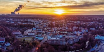 Luftbild einer Lausitzer Stadt im Sonnenuntergang, am Horizont die Kühltürme eines Kraftwerks