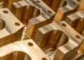 Mehrere frisch gefräste Metallbauteile mit Bohrungen und glänzenden Oberflächen liegen nebeneinander