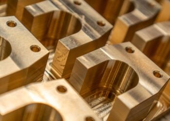Mehrere frisch gefräste Metallbauteile mit Bohrungen und glänzenden Oberflächen liegen nebeneinander