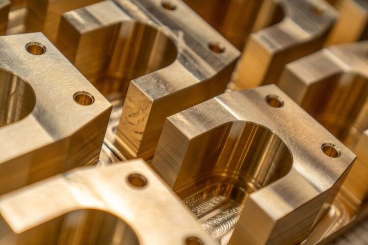 Mehrere frisch gefräste Metallbauteile mit Bohrungen und glänzenden Oberflächen liegen nebeneinander
