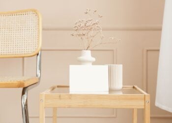Kleiner Beistelltisch aus Holz mit Glasplatte, darauf eine Keramikvase mit Trockenblumen, daneben ein Freischwinger